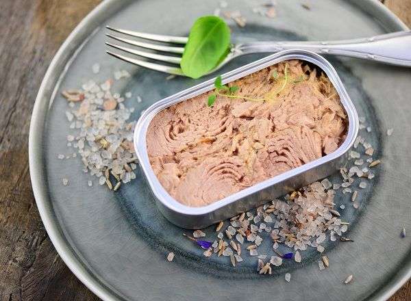 Atún escabechado en lata sobre plato con tenedor en mesa de madera