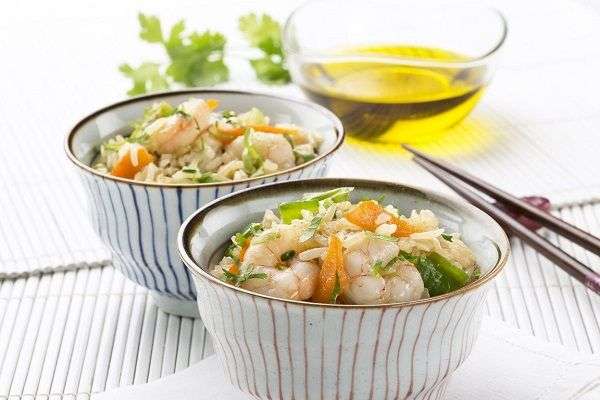 Aceitera, palillos y dos boles blancos de rayas con arroz salteado con gambas y verduras. 