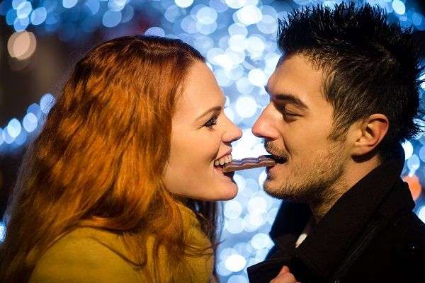 Pareja comiendo un trozo de chocolate entre los dos con fondo difuminado