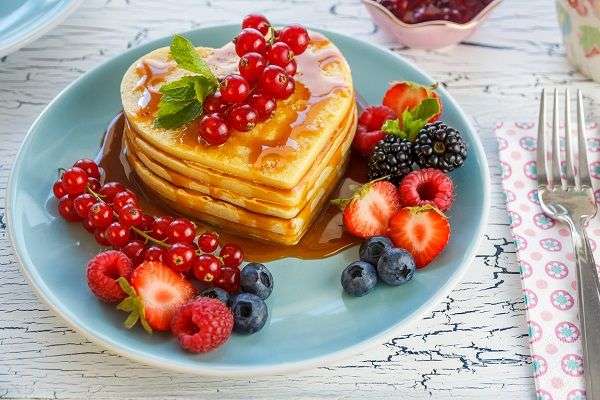 Tortitas con fresas, arándanos y caramelo sobre plato azul en mesa de madera