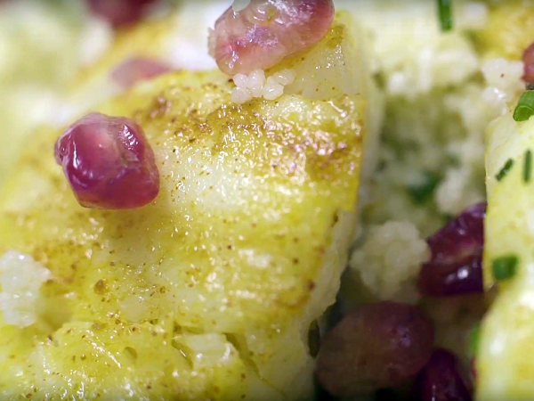 Plato blanco con bacalao marinado con cuscús y granada sobre madera