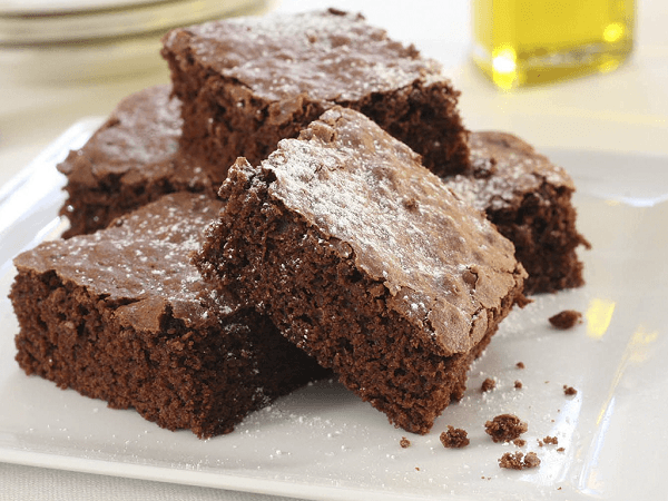 Brownies de chocolate en plato blanco con azúcar glas. En fondo, botella de aceite 