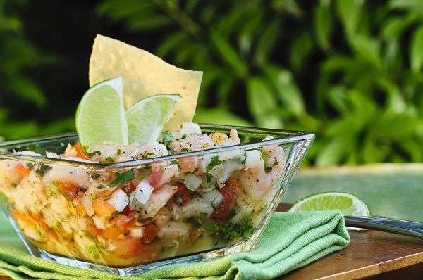 Ceviche de camarón y pulpo en vaso de cristal transparente sobre mantel verde al aire libre. 