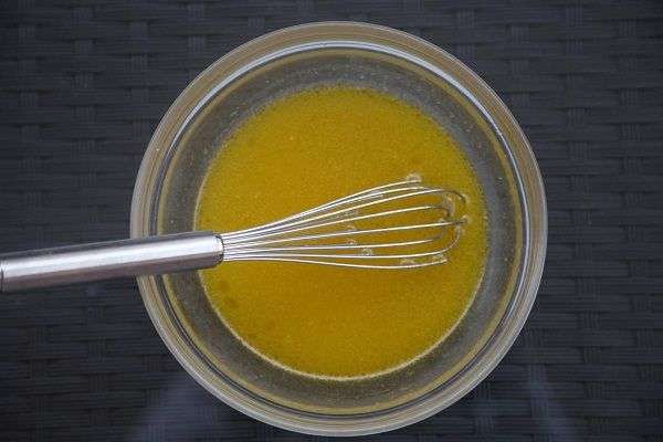Bol de cristal transparente con una varilla y con aliño de zumo de naranja, limón y lima, aceite de oliva y sal sobre mesa marrón