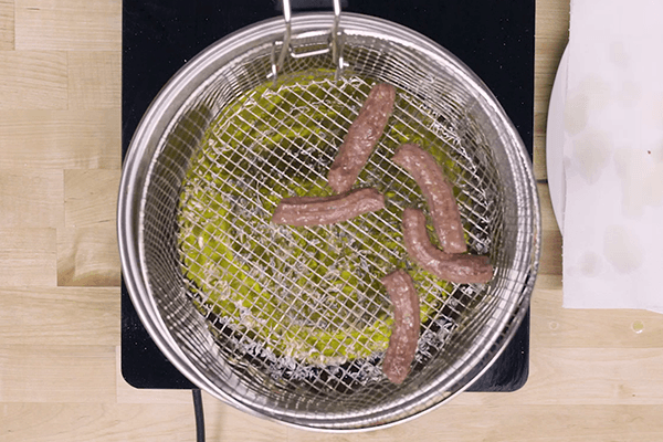 Sartén con aceite de oliva caliente y cesta con churros sobre hornillo eléctrico sobre tabla de madera