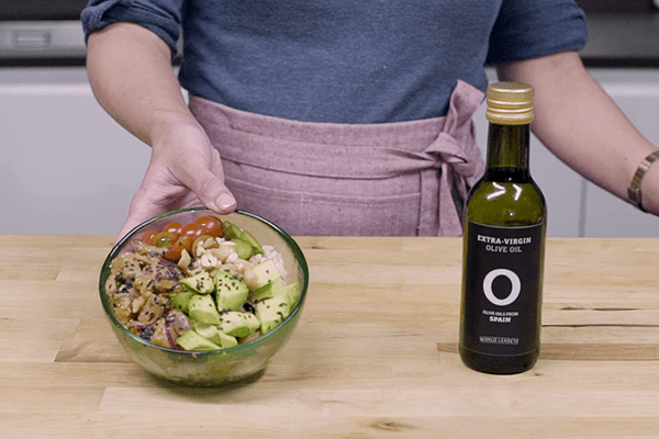 Ensalada poke en cuenco sobre mesa de madera y botella de aceite de oliva 