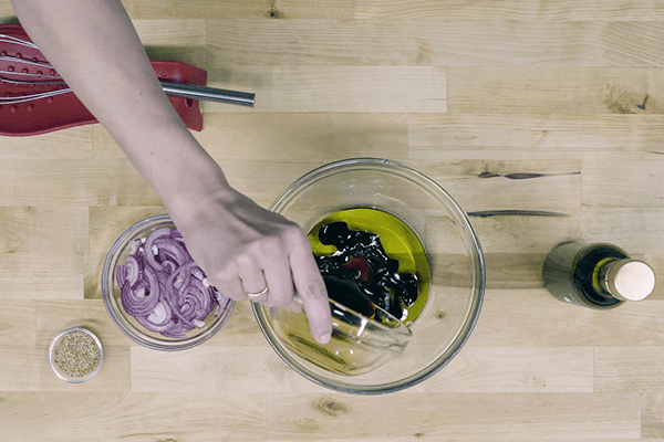 Mano vertiendo salsa de soja en recipiente con aceite de oliva virgen extra sobre tabla de madera