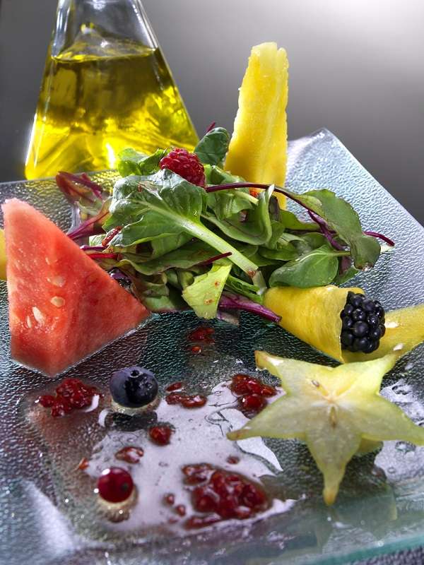 Plato de cristal con ensala de frutas de temporada y aceite de oliva