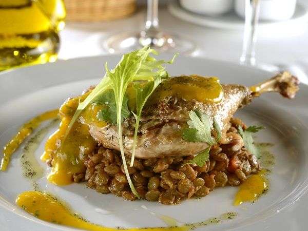 Plato blanco con muslo de pato sobre lentejas estofadas