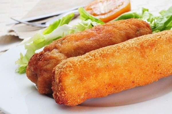 Plato blanco con flamenquín con ensalada sobre mesa con servilleta y cubiertos