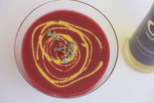 Gazpacho de remolacha en vaso de cristal y botella de aceite sobre fondo blanco