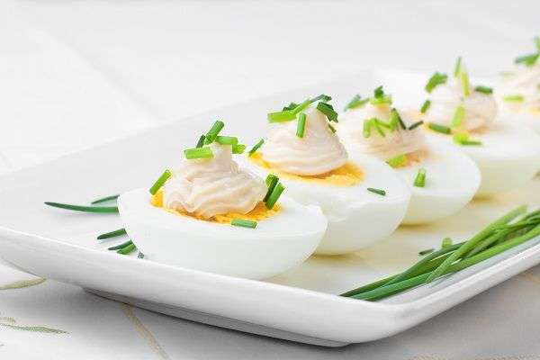 planto blanco con huevos duros cortados por la mitad con mayonesa y decorados con cebollino sobre mesa con mantel de tela blanco