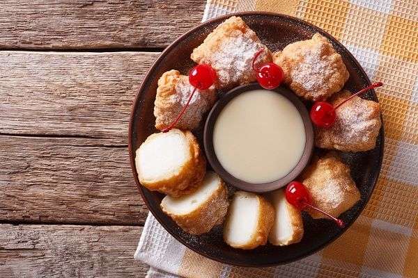 Plato negro con leche frita con guindas sobre fondo de madera