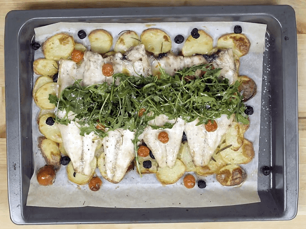 Bandeja de horno sobre mesa de madera con lubina con romero, aceitunas negras y tomates cherry con base de patata