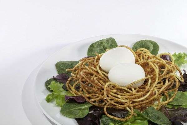 espaguetis con huevo duro sobre mezcla de lechugas en plato blanco sobre fondo blanco