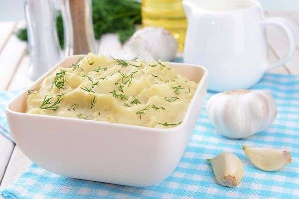 Puré de patata adornado con hierbas aromáticas en cuenco blanco sobre mantel de cuadros azules