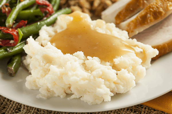 Puré de patata con salsa gravy con verduras y carne mechada en plato blanco sobre mantel de mimbre