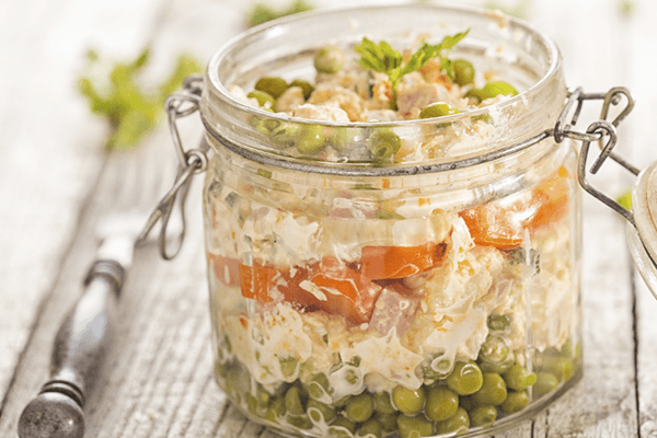 Tarro de cristal abierto con ensaladilla rusa sobre mesa de madera