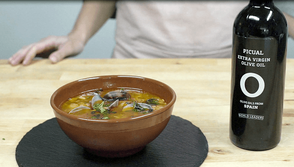 bandeja de pizarra con cuenco de barro con sopa de almejas al estilo Manhattan con una botella de aceite de oliva sobre mesa de madera