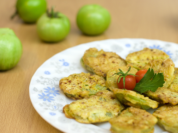 Mesa de madera con tomates verdes y plato blanco con tomates verdes fritos