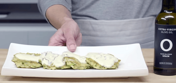 Mano mostrando plato blanco con tortitas de calabacín con salsa de yogur.