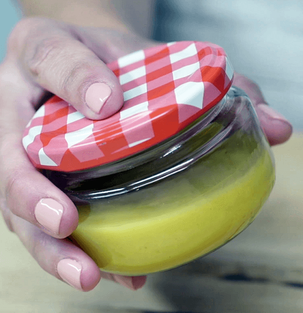 Mano mostrando tarro de cristal con tapa de rosca de cuadros rojos y blancos con salsa de mostaza 