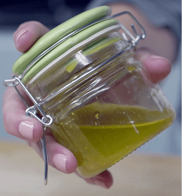 Mano mostrando tarro de cristal con tapa verde con vinagreta de naranja