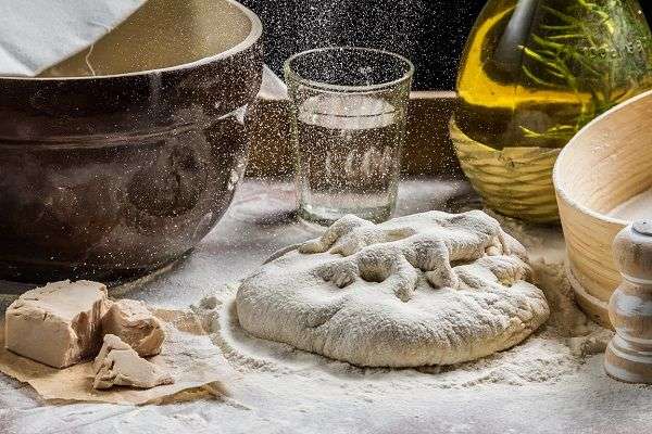 Masa para pizza, levadura, botella de aceite, sal sobre mesa llena de harina